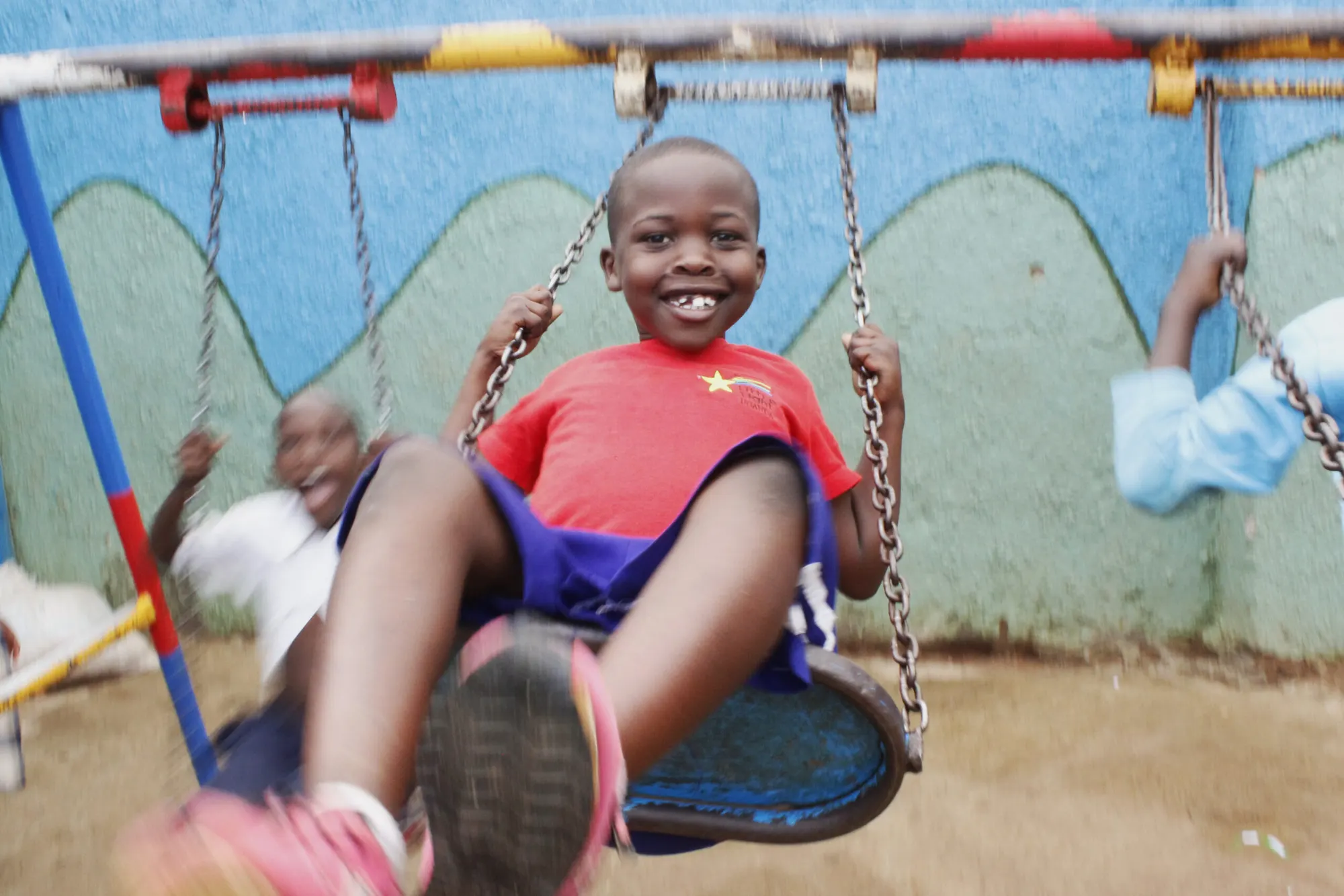A smiling boy on a swing in the playground at Little Light Children Center in Namuwongo, Kampala