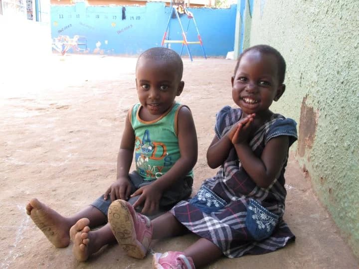 Two smiling nursery children sitting in the Little Light courtyard