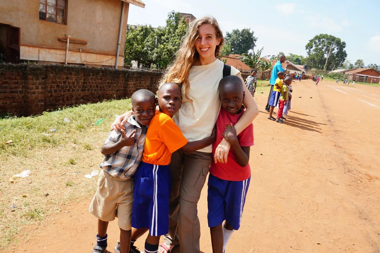 A volunteer with her arms around three smiling boys on the dirt field next to Little Light Children Center